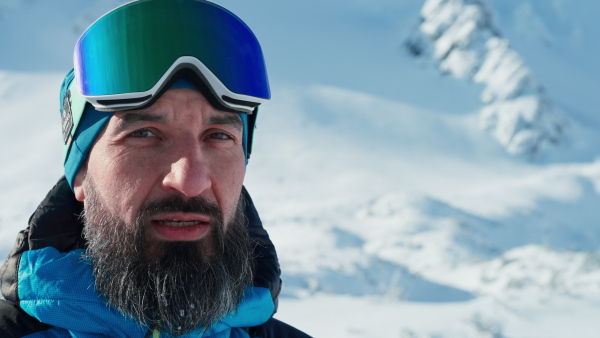 A close-up of alpine skier looking at camera in snowy mountains.