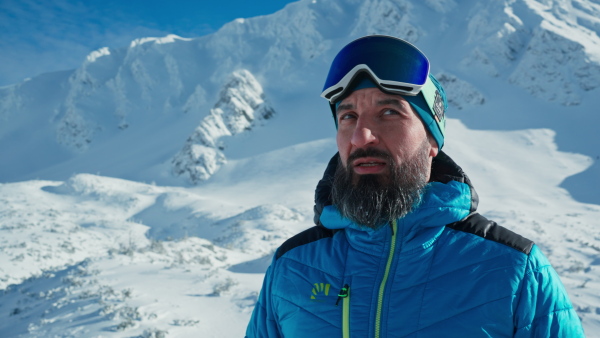 A close-up of alpine skier looking at camera in snowy mountains.