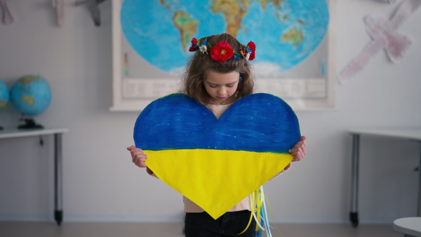 A little Ukrainian schoolgirl holding heart in Ukrainian colors and looking at camera at school.