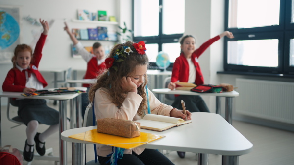 A little sad Ukrainian girl writing in classroom during class, concept of enrolling Ukrainian kids to schools.