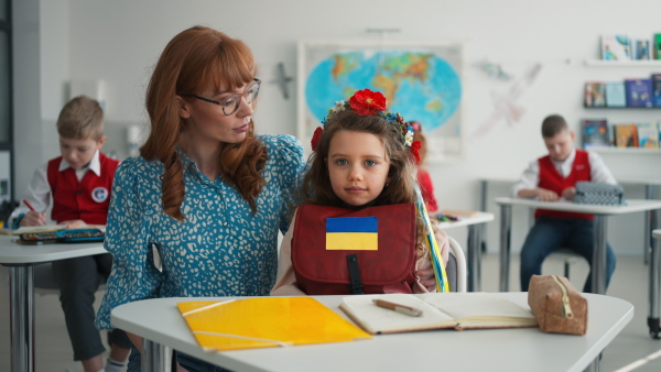 A teacher with Ukrainian schoolgirl in classroom, concept of enrolling Ukrainian kids to schools.