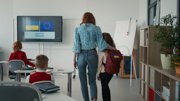 A rear view of teacher with Ukrainian schoolgirl in classroom, concept of enrolling Ukrainian kids to schools.