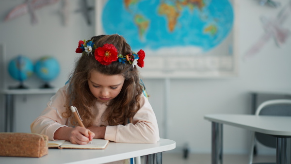 A little sad Ukrainian girl sitting in classroom during class, concept of enrolling Ukrainian kids to schools.