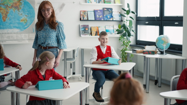 A teacher walking through class and watching children using digital tablets during lesson at primary school.