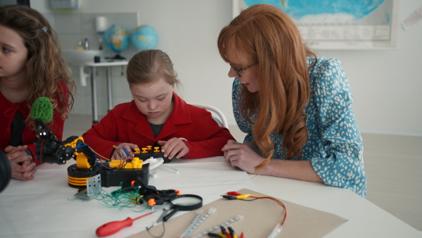 A young teacher is private tutoring little student with Down syndrome during robotics class at school.