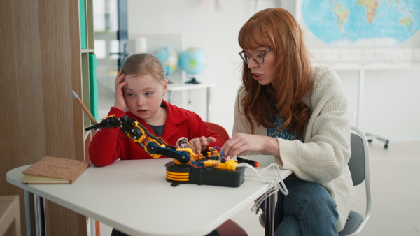 A young teacher is private tutoring little student with Down syndrome during robotics class at school.