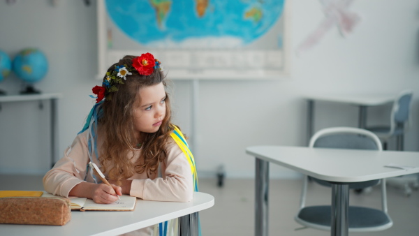 A little sad Ukrainian girl sitting in classroom during class, concept of enrolling Ukrainian kids to schools.