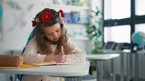 A little sad Ukrainian girl sitting in classroom during class, concept of enrolling Ukrainian kids to schools.