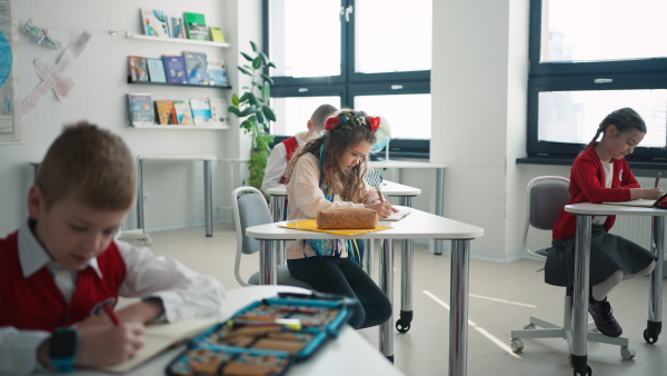 A little sad Ukrainian girl writing in classroom during class, concept of enrolling Ukrainian kids to schools.