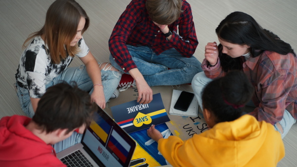 Teenage students sitting at circle in a classroom with posters to support Ukraine, no war concept.