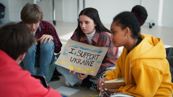 Teenage students sitting at circle in a classroom with posters to support Ukraine, no war concept.