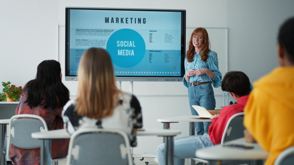 Happy young High school teacher giving marketing lesson to students in classroom