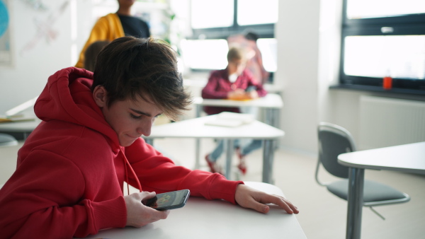 A teenage student using smartphone at classroom during break.