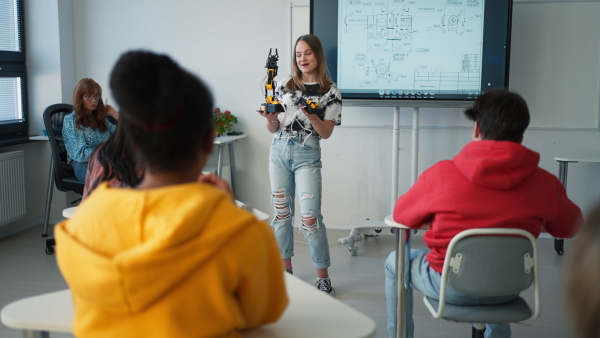 A college student presenting her builded robotic toy to young science teacher at robotics classroom at school.