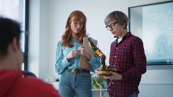 A college student presenting his builded robotic toy to young science teacher at robotics classroom at school.