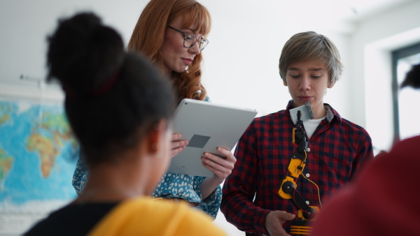 Cheerful students showing their builded robotic toy to a young science teacher at robotics classroom at school.