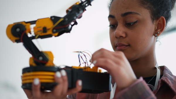 A college student holding her robotic toy at robotics classroom at school.