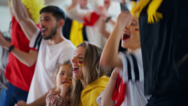 Excited football fans, mother with little daughter, supproting a German national team in live soccer match at stadium.