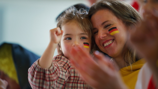 Excited football fans, mother with little daughter, supproting a German national team in live soccer match at stadium.