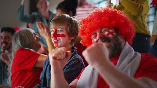 Excited football fans supproting an English national team in live soccer match at stadium.