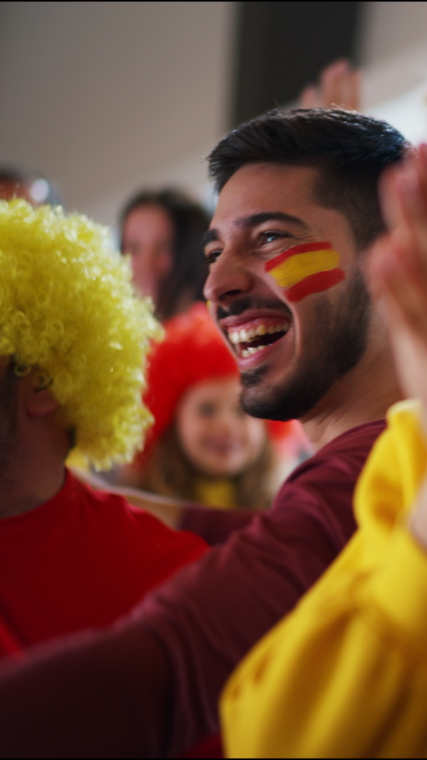 A vertical footage of excited football fans supproting Spanish national team in live soccer match at stadium.