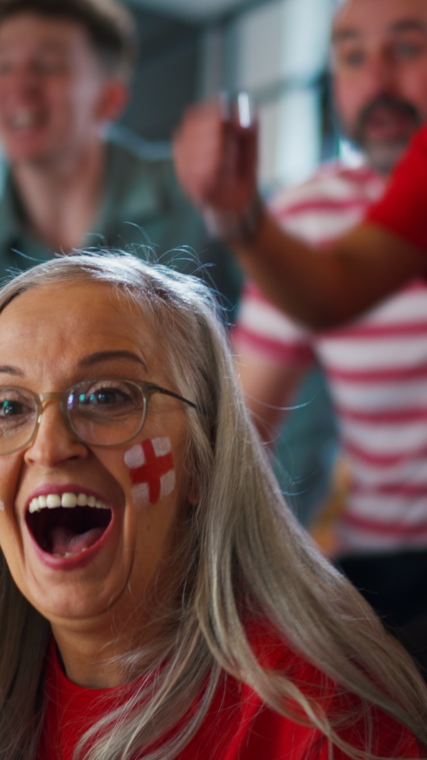 A vertcial footage of excited senior woman football fan supproting English national team in live soccer match at stadium.