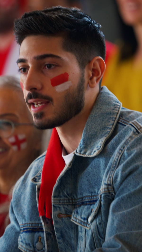 Excited senior woman and young man football fans supproting English national team in a live soccer match at stadium.