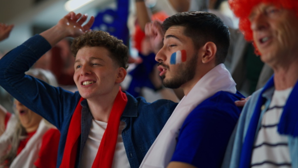 Excited football fans supproting French national team in live soccer match at astadium.