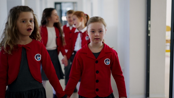 A happy schoolgrirl with Down syndrome in uniform walking in scool corridor with classmates behind her.