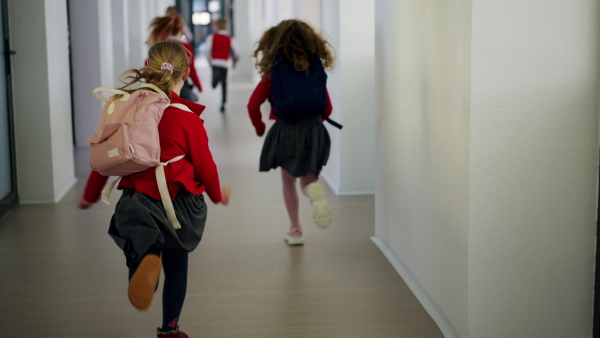 A rear view of schoolchildren in uniforms running in school corridor.