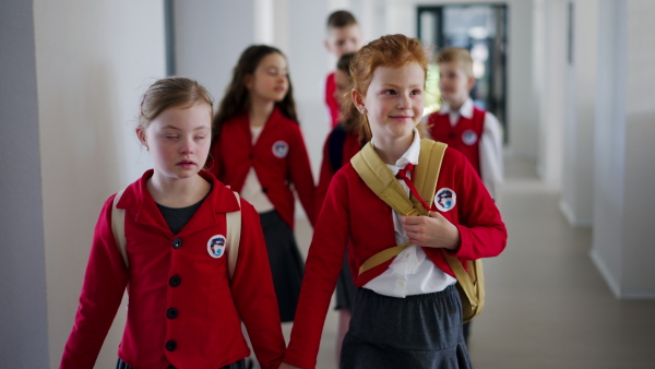 A happy schoolgrirl with Down syndrome in uniform walking in scool corridor with classmates behind her.