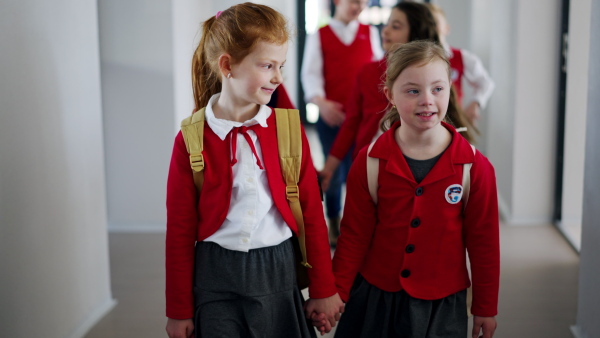 A happy schoolgrirl with Down syndrome in uniform walking in scool corridor with classmates behind her.