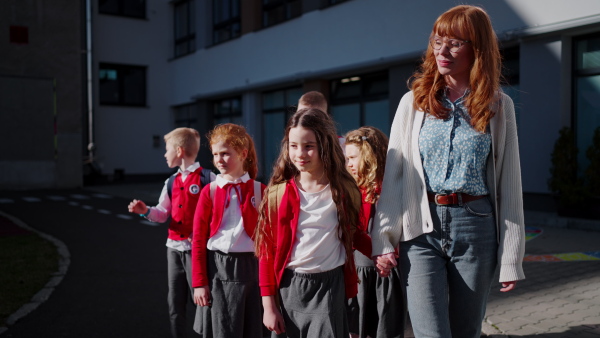 Happy schoolkids in uniforms with teacher walking at a schoolyard.