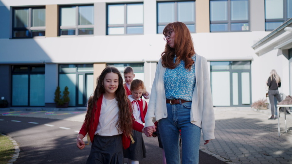 Happy schoolkids in uniforms with teacher walking at schoolyard.