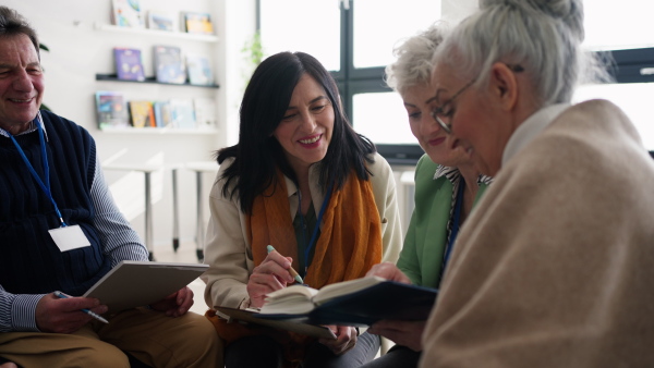 Excited elderly people attending a group therapy session at nursing house, positive senior man and woman sitting in circle, having conversation with psychologist