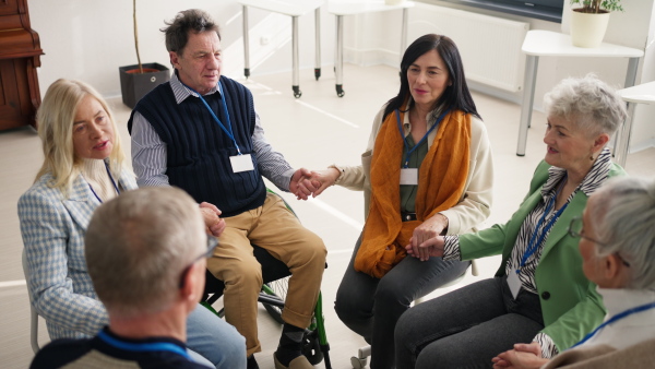 A group of senior people sitting in circle during therapy session, holding hands and praying together.