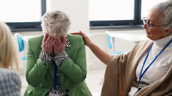 A group of senior people sitting in circle during therapy session, consoling depressed woman.