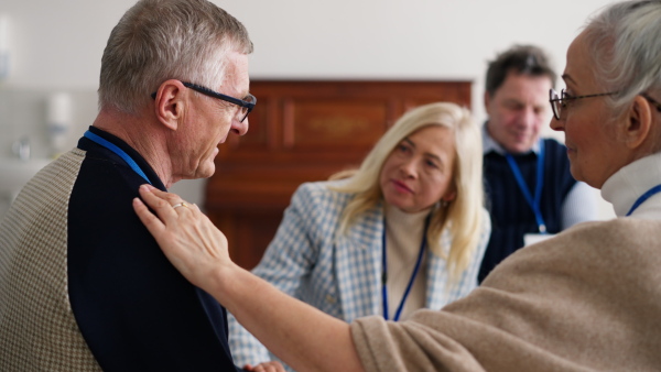 A group of senior people sitting in circle during therapy session, woman consoling depressed man.