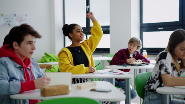 High school students paying attention in class, sitting in their desks and raising hands.