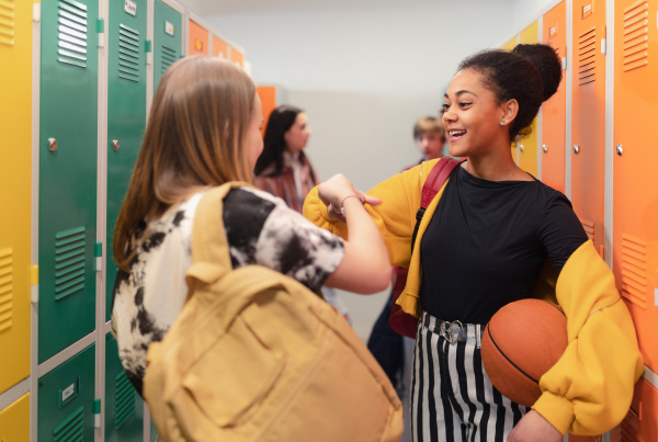 Young high school students meeting and greeting near a locker in campus hallway talking and high fiving.