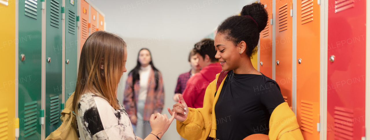 Young high school students meeting and greeting near a locker in campus hallway talking and high fiving.