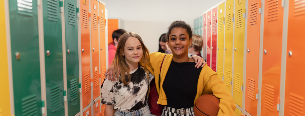 Young high school students meeting and greeting near a locker in campus hallway talking and high fiving.