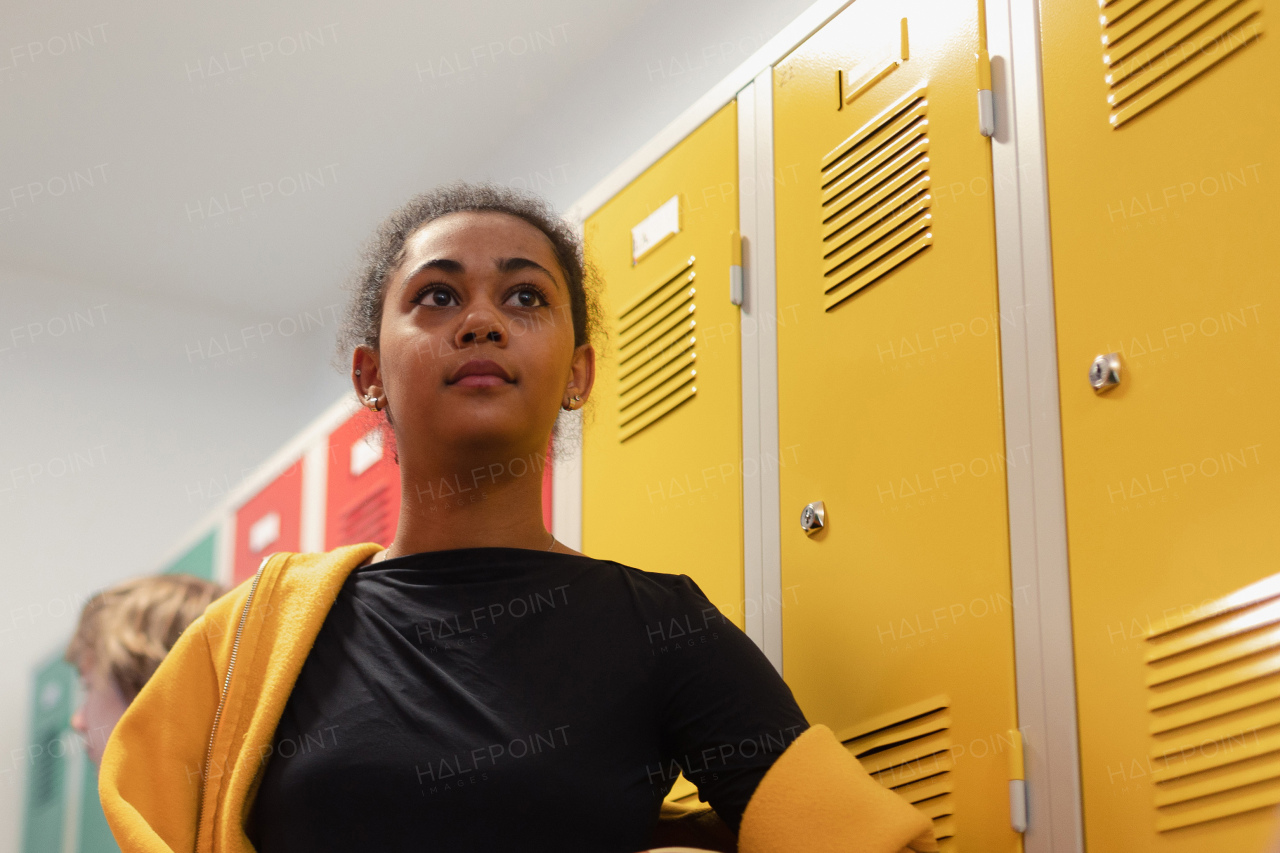 Multiracial girl standing with a basketball ball in locker room with her classmates in background. Low angle view.