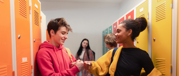 Young high school students meeting and greeting near a locker in campus hallway talking and high fiving.