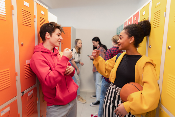 Young high school students meeting and greeting near a locker in campus hallway talking and high fiving.