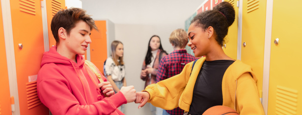 Young high school students meeting and greeting near a locker in campus hallway talking and high fiving.