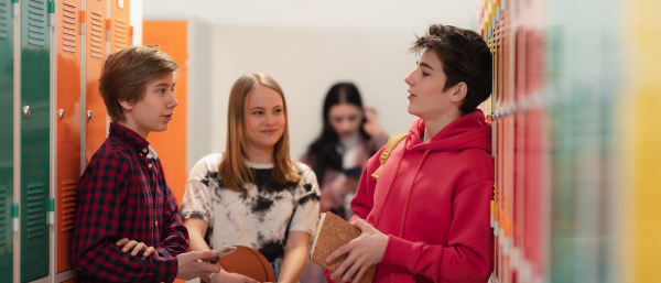 Young high school students meeting and greeting near locker in a campus hallway, back to school concept.