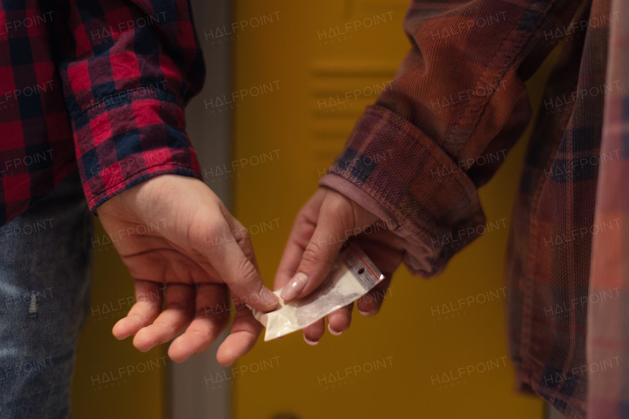 Unrecognizable high school students dealing drugs in a shool corridor.