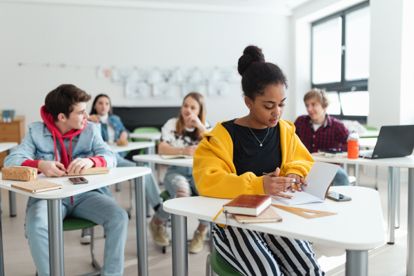 High school students paying attention in a class, sitting in their desks and writing notes, back to school concept.