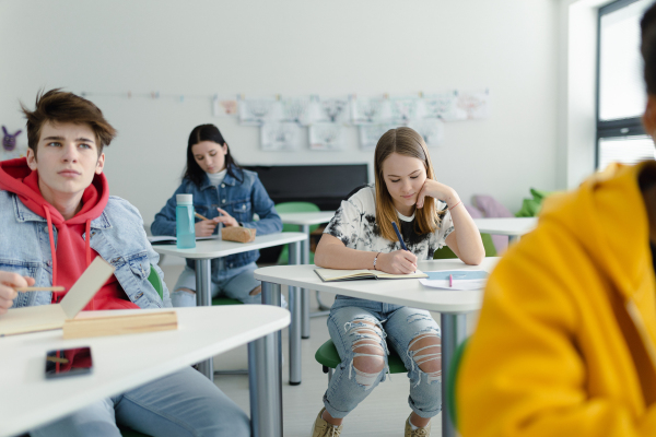 High school students paying attention in a class, sitting in their desks and writing notes, back to school concept.